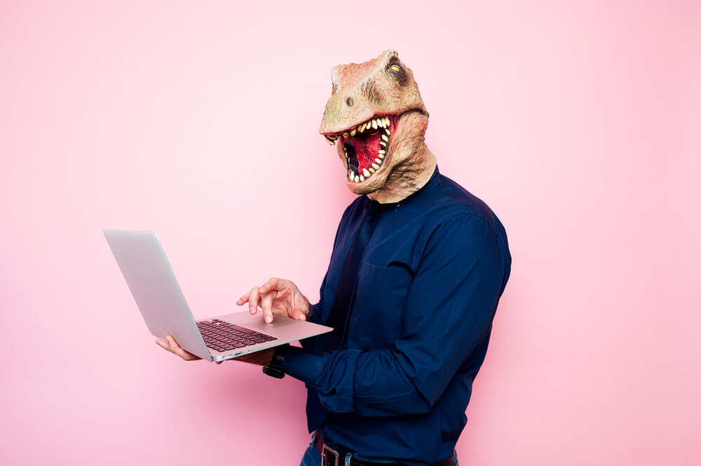 Person mit Dinosauriermaske auf dem Kopf hält Laptop in den Händen