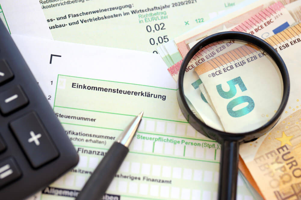 Steuererklärung mit Lupe und Taschenrechner auf Geldscheinen.