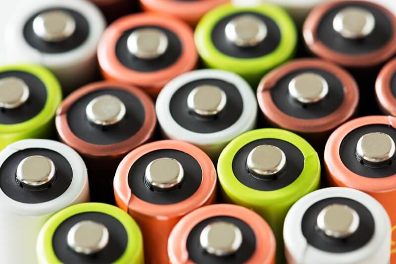 Mehrere eng nebeneinanderliegende Batterien von oben gesehen, mit sichtbaren Pluspolen und verschiedenfarbigen Ummantelungen in Weiß, Orange, Grün und Braun.